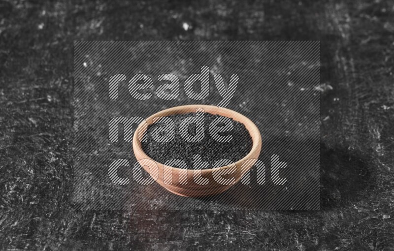 وعاء خشبي ممتلئ ببذور حبة البركة علي خلفية سوداء