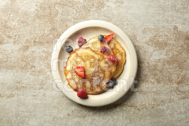 Three stacked mixed berries pancakes in a grey plate on beige background