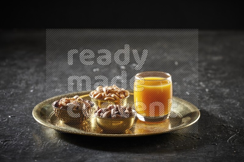 مكسرات في أطباق معدنية مع مشروب قمر الدين على صينية علي خلفية سوداء