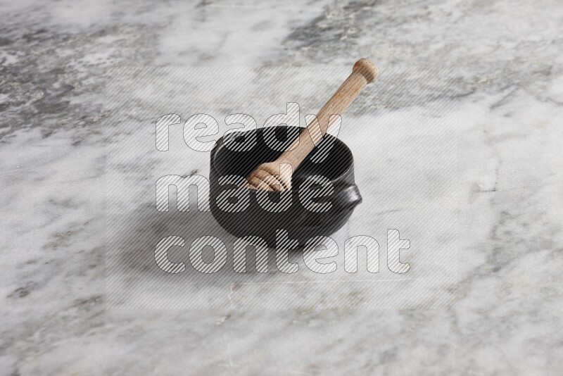 Black pottery bowl with wooden honey dipper in it on grey marble background
