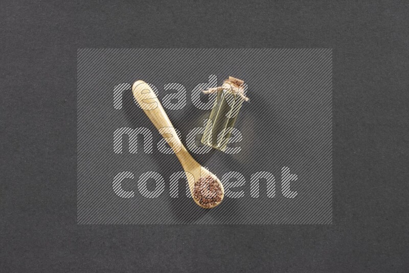 A wooden spoon full of flaxseeds with a glass bottle of flaxseeds oil on a black flooring