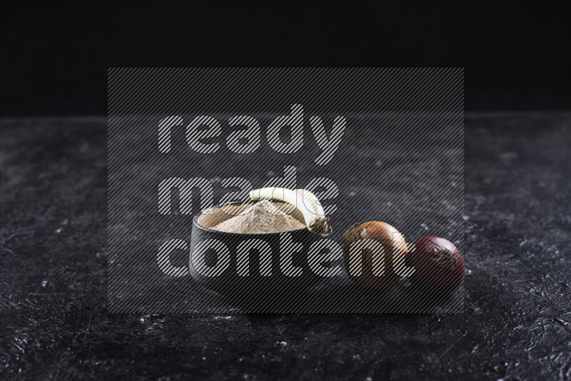 A black pottery bowl full of onion powder on black background