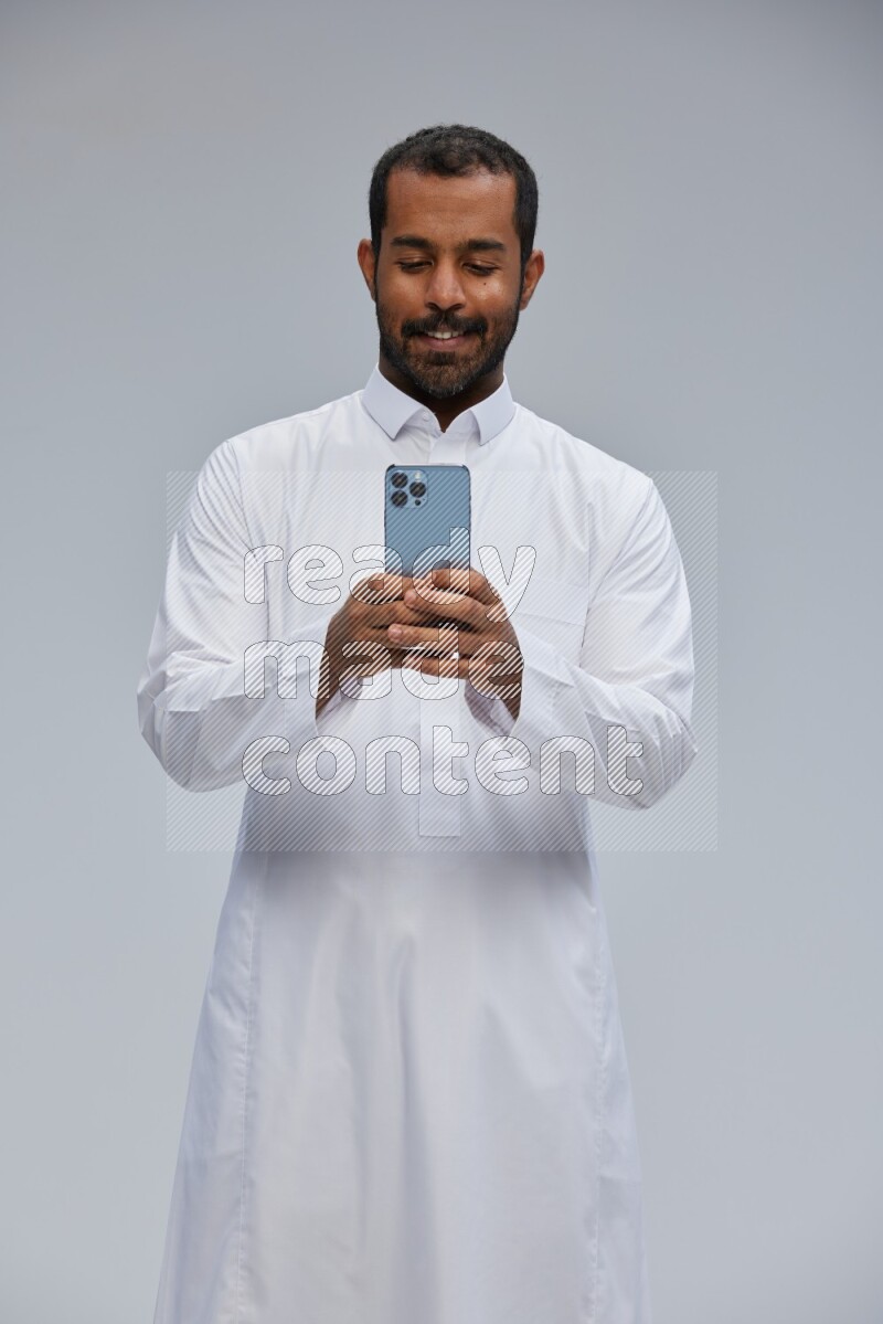 Saudi man wearing Thob standing texting on phone on Gray background
