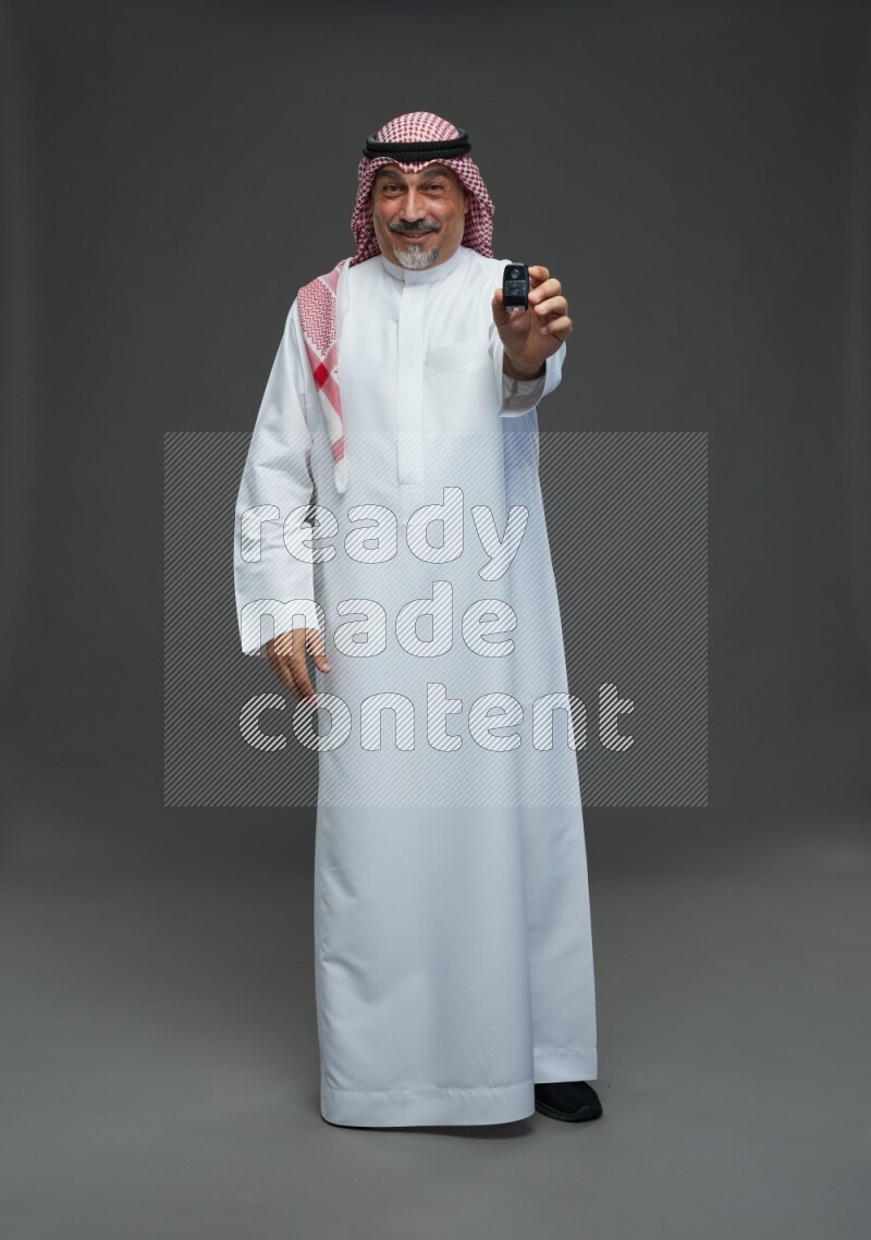 Saudi man with shomag Standing holding car key on gray background