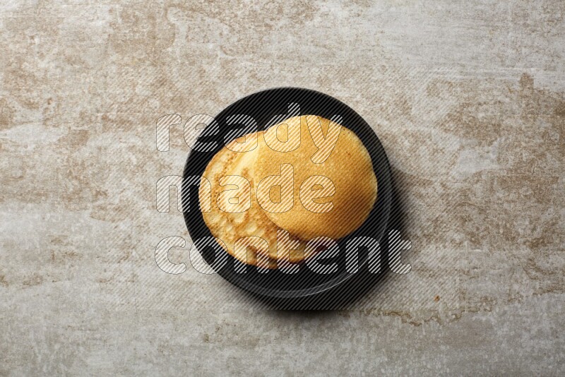 Three stacked plain pancakes in a black plate on beige background
