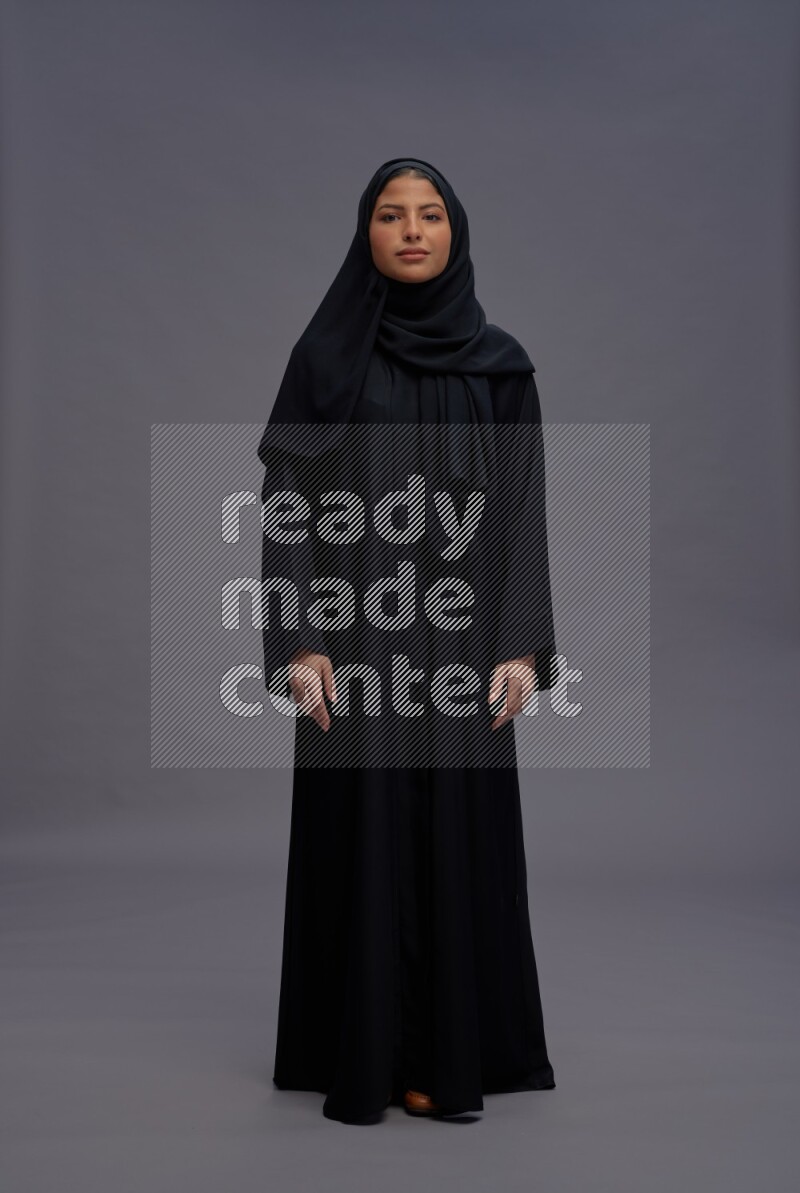 Saudi woman wearing Abaya standing interacting with the camera on gray background