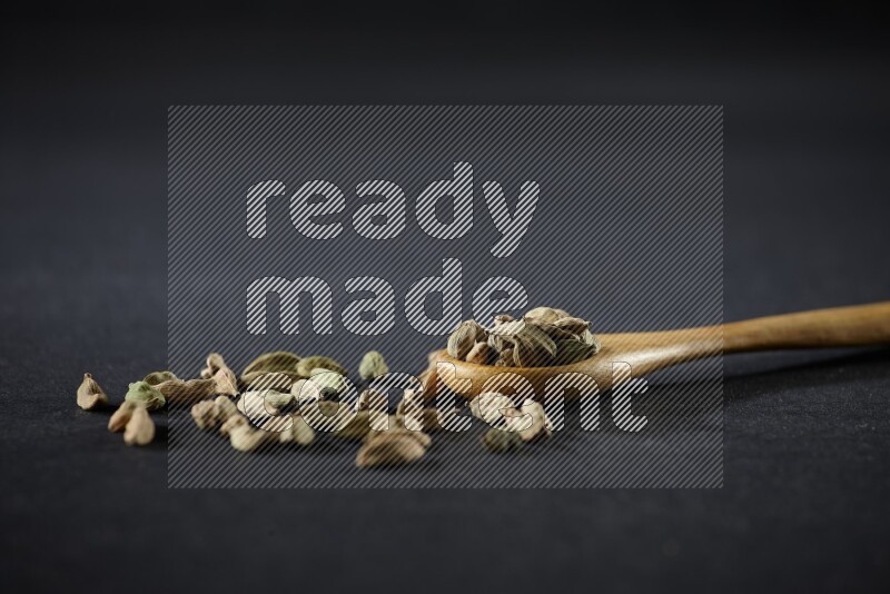 ملعقة خشبية ممتلئة بالهيل على خلفية سوداء