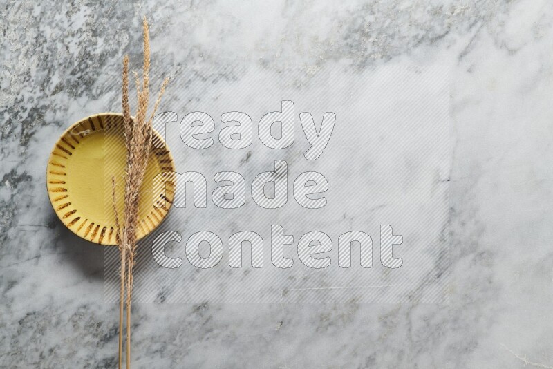 Wheat stalks on multicolored pottery plate on grey marble background