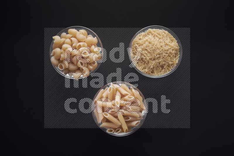 Different pasta types in glass bowls on black background