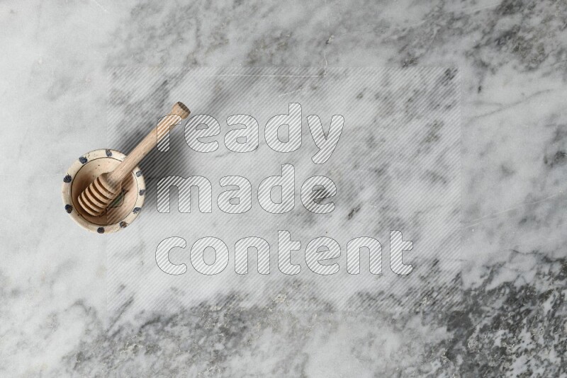 Decorative pottery bowl with wooden honey dipper in it on grey marble background