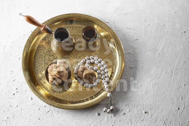 Dried figs in a metal bowl with coffee and prayer beads on a tray in a light setup