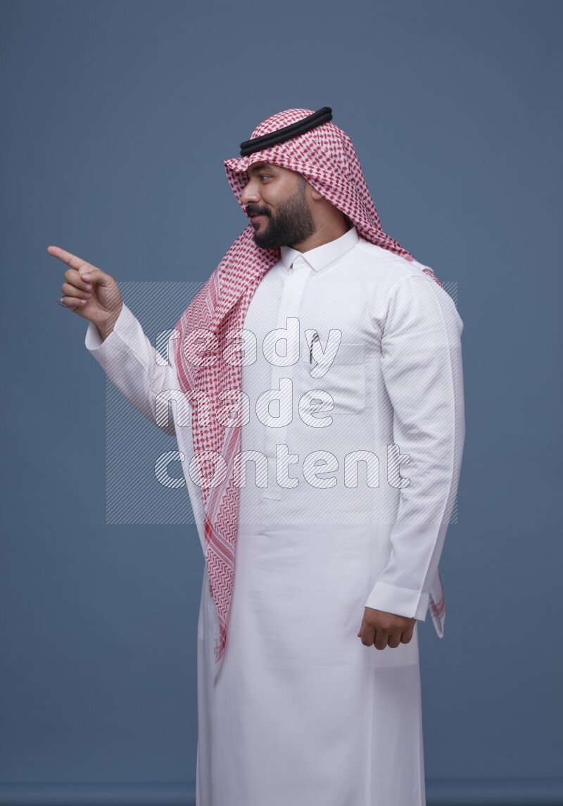 A Saudi man posing on blue background wearing Thob and Shomag