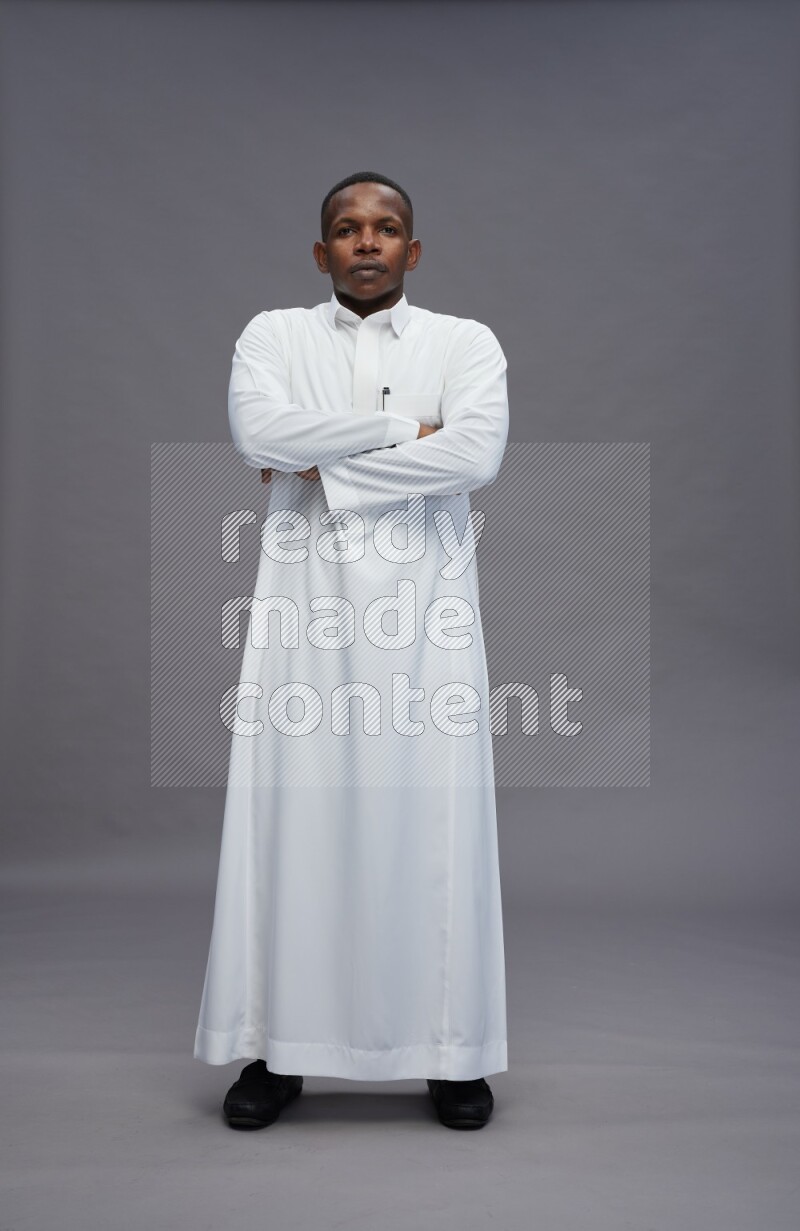 Saudi man wearing thob standing with crossed arms on gray background