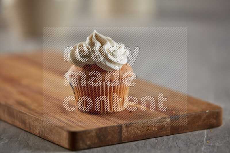 Vanilla cupcake topped with cream on a wooden board