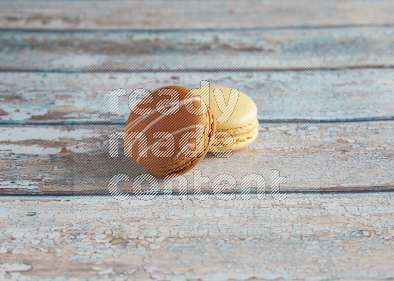 45º Shot of of two assorted Brown Irish Cream, and Yellow Vanilla macarons on light blue background
