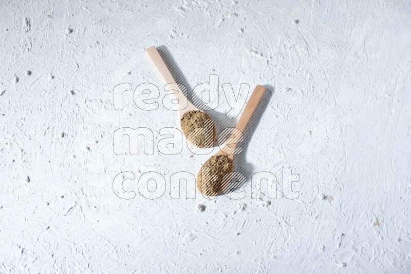Wooden spoons full of allspice powder and allspice whole balls spreaded on a textured white flooring