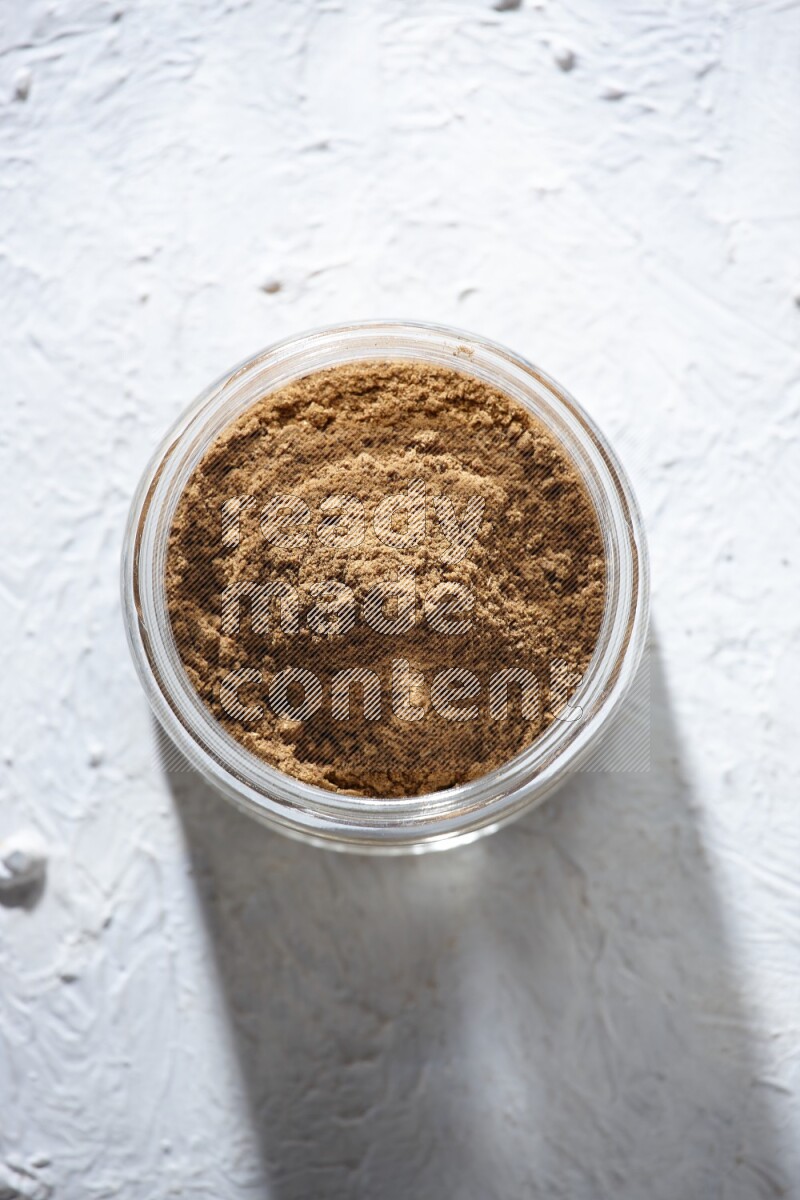 A glass jar full of allspice powder on a textured white flooring
