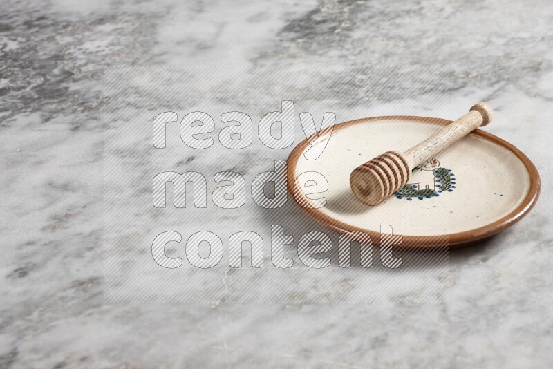 Decorative pottery plate with wooden honey dipper in it on grey marble background