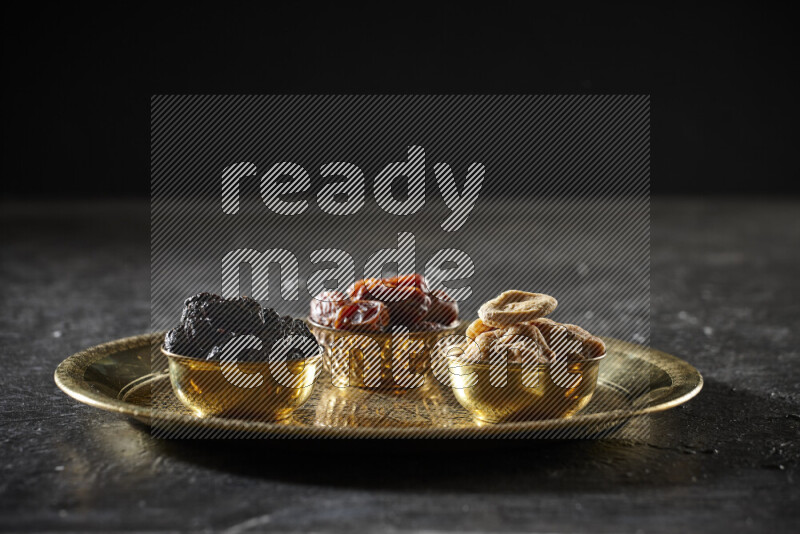 Dried fruits in metal bowls on a tray in a dark setup