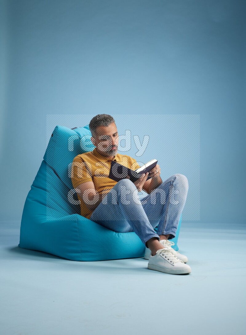 A man sitting on a blue beanbag and reading a book