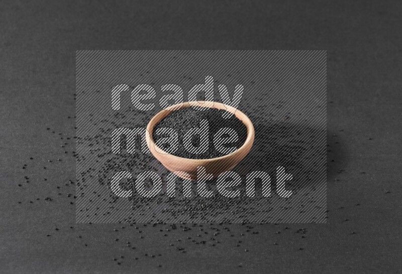 وعاء خشبي ممتلئ ببذور حبة البركة محاط ببعض البذور علي خلفية سوداء