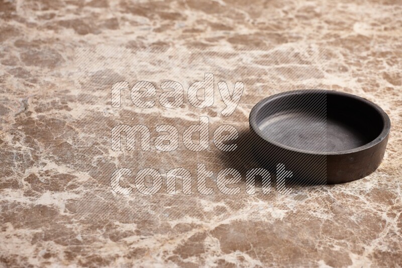 A black pottery bowl on beige marble background