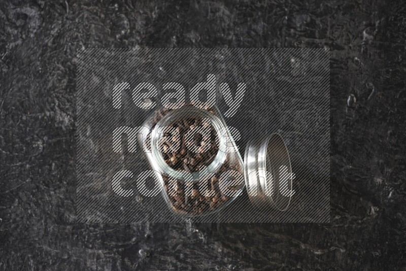 A glass spice jar full of cloves on textured black flooring