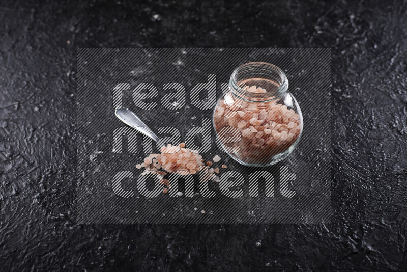 A glass jar full of coarse himalayan salt crystals on black background