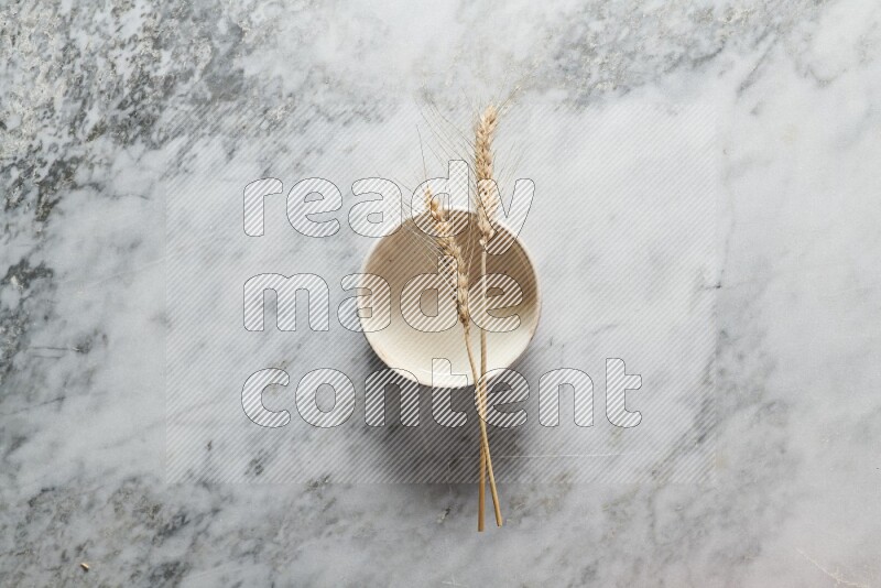 Wheat stalks on beige pottery bowl on grey marble background
