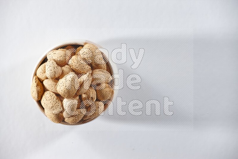 A beige ceramic bowl full of almonds on a white background in different angles