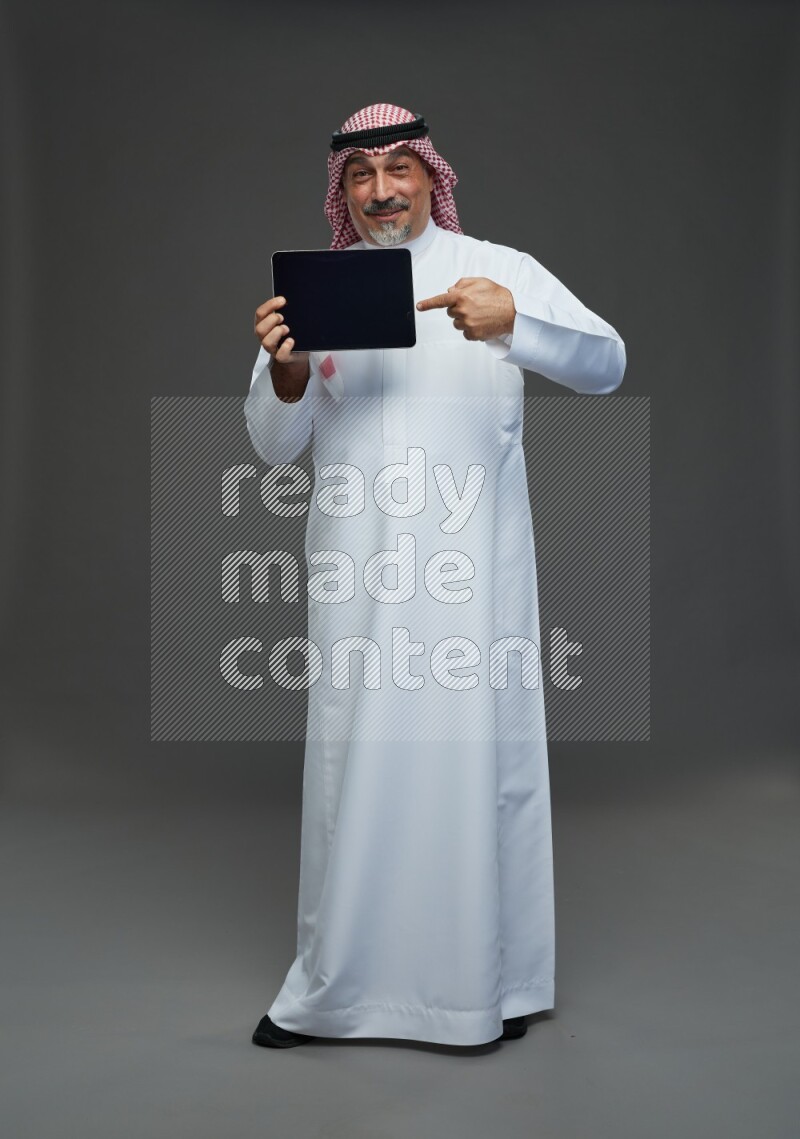 Saudi man with shomag Standing working on tablet on gray background