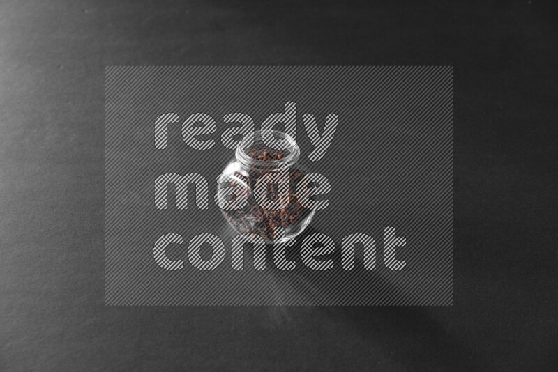 A glass spice jar full of cloves on black flooring