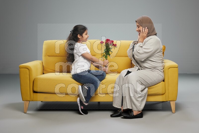 A girl sitting giving flowers to her mother on gray background