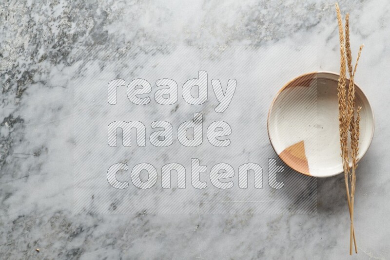Wheat stalks on multicolored pottery plate on grey marble background