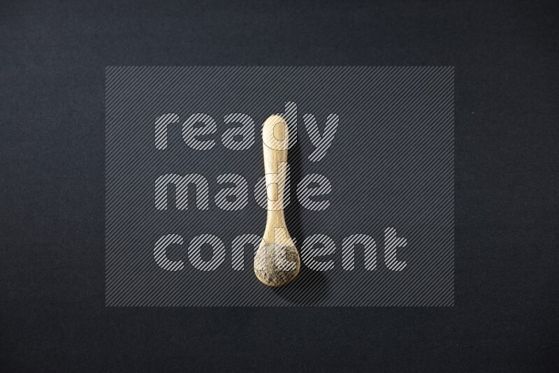 A wooden spoon full of cardamom powder on black flooring