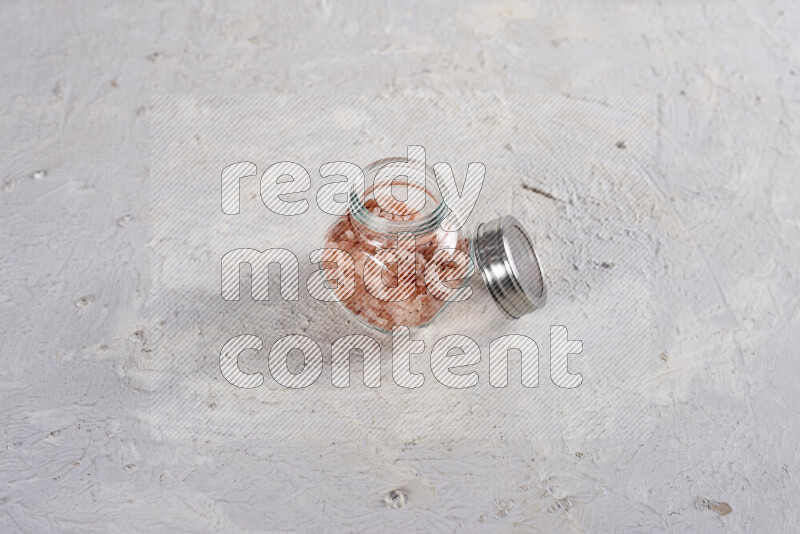 A glass jar full of coarse himalayan salt crystals on white background