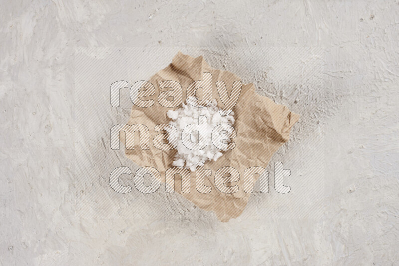 A crumpled piece of paper full of white salt on white background