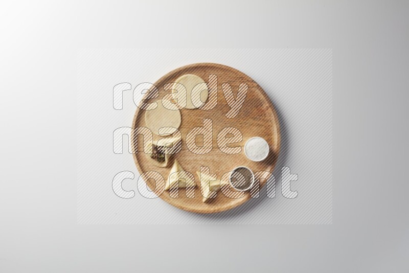 two closed sambosas and one open sambosa filled with meat while salt and black pepper aside in a wooden dish on a white background