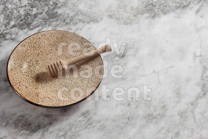 Multicolored pottery plate with wooden honey dipper in it on grey marble background