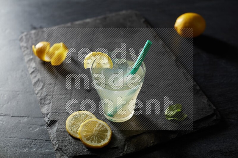 A glass of lemon juice with a straw on black background