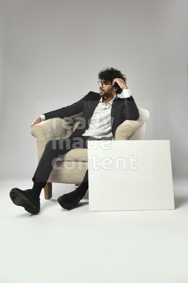 A man wearing formal sitting on a chair holding a white board on white background
