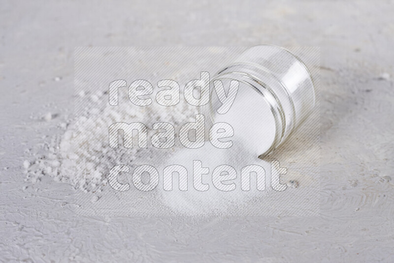 A glass jar full of table salt with some sea salt crystals beside it on a white background