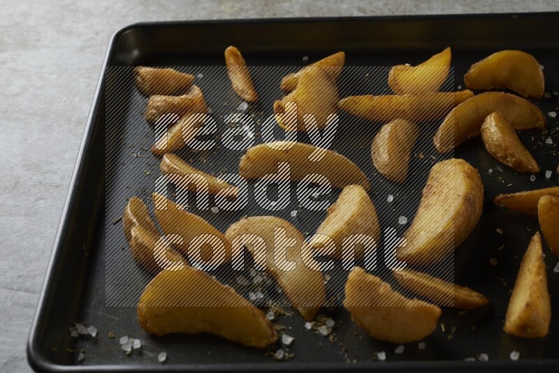 wedges potato in a black stainless steel rectangle tray on grey textured counter top