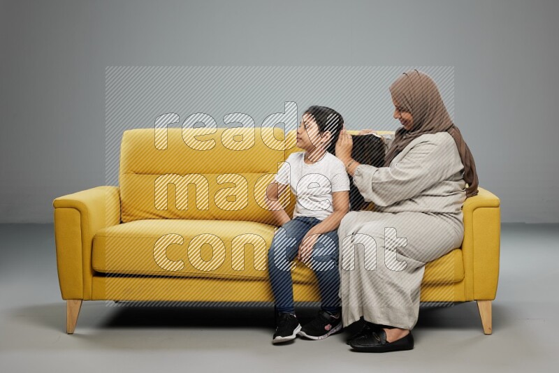 A mother sitting styling hair for her daughter on gray background