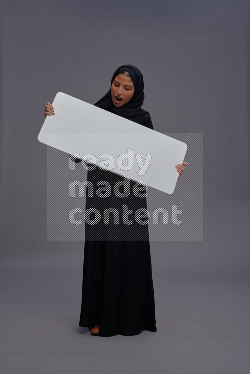 Saudi woman wearing Abaya standing holding white board on gray background