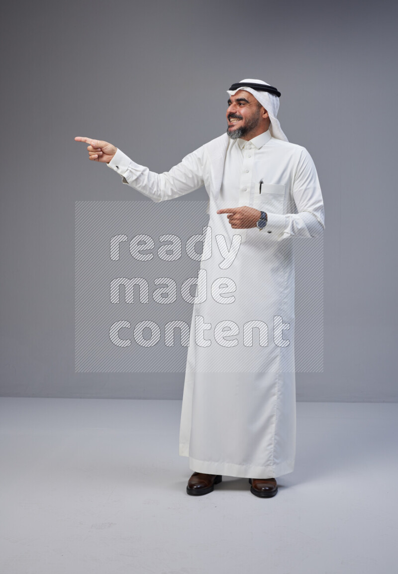 Saudi man Wearing Thob and white Shomag standing interacting with the camera on Gray background