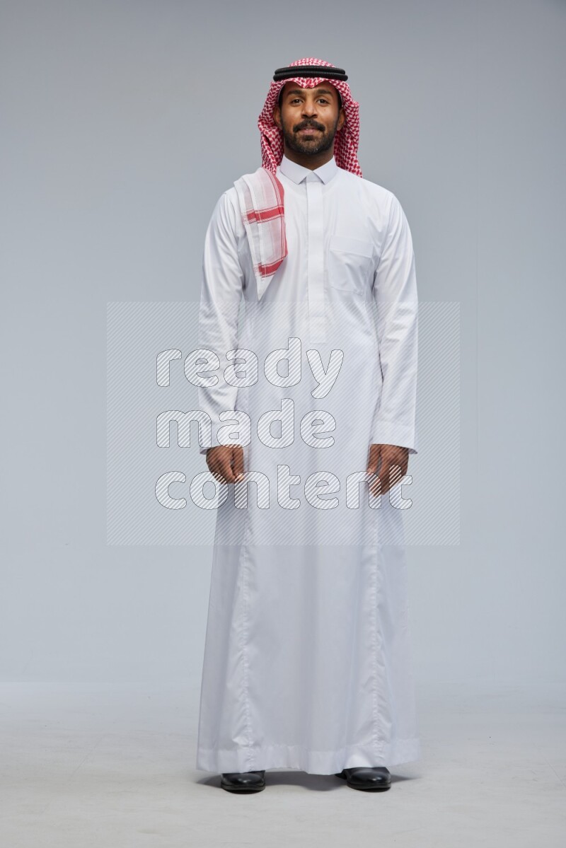 Saudi man Wearing Thob and shomag standing interacting with the camera on Gray background