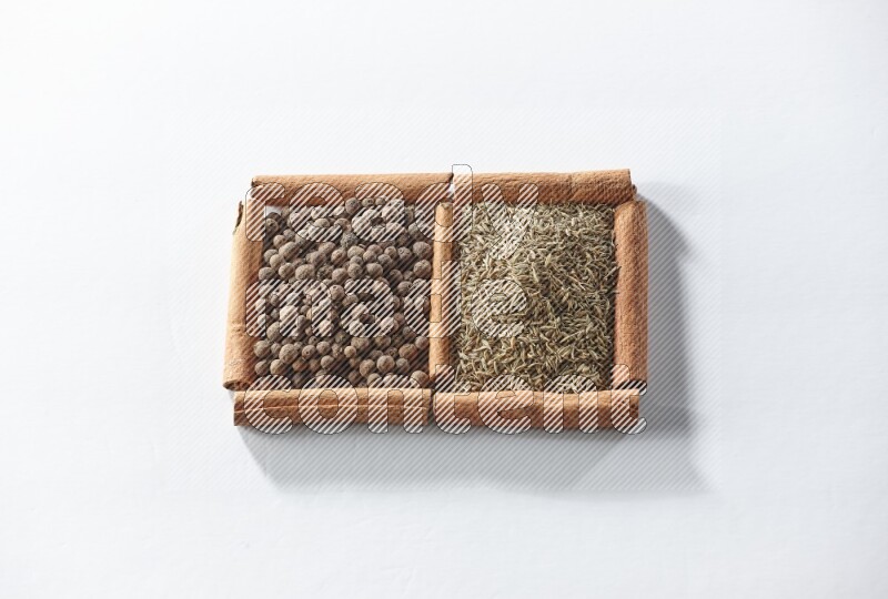 مربعان من أعواد القرفة ممتلئان ببهار الفلفل الحلو والكمون علي خلفية بيضاء