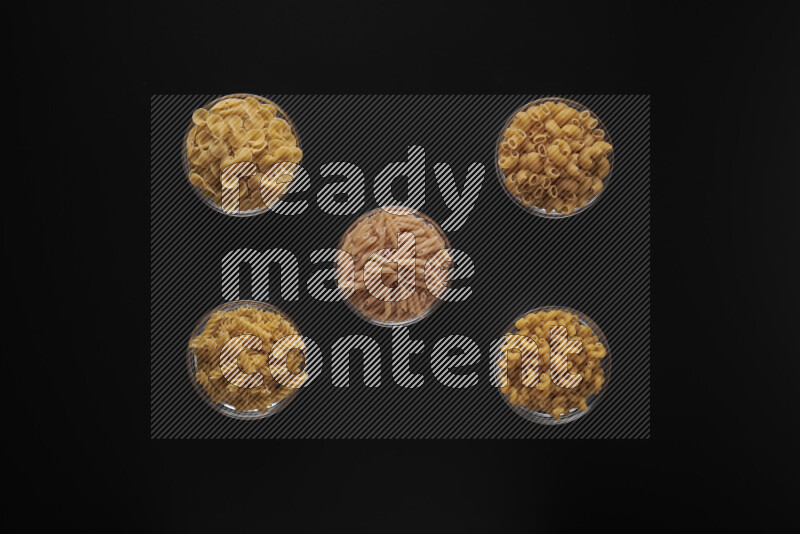 Different pasta types in 5 glass bowls on black background