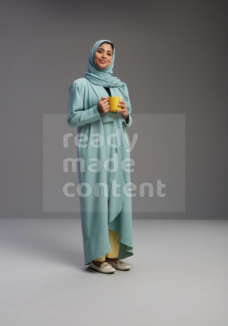 Saudi Woman wearing Abaya standing  holding a mug on Gray background